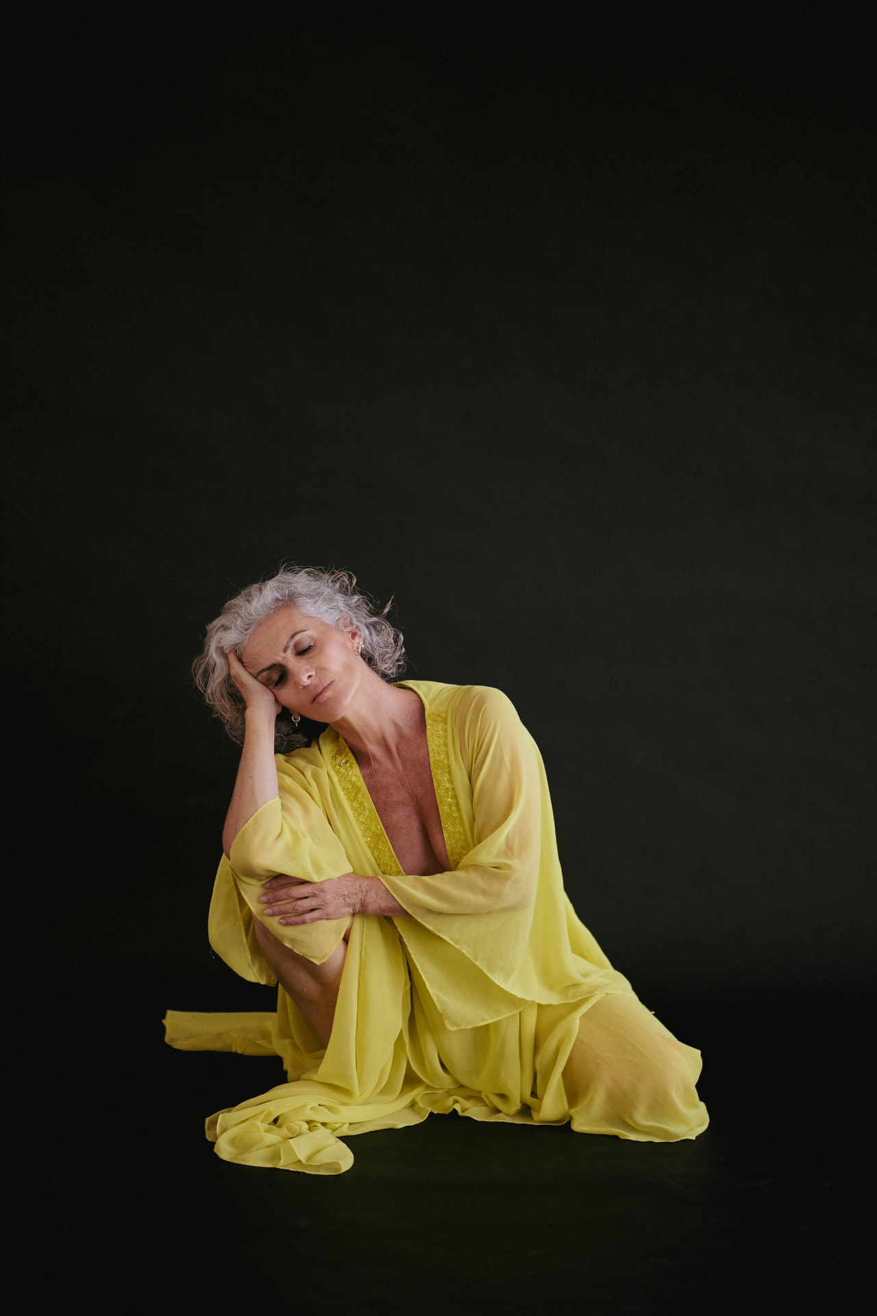 Emmanuelle Em seated in a yellow dress, head resting on her hand, deep in contemplation