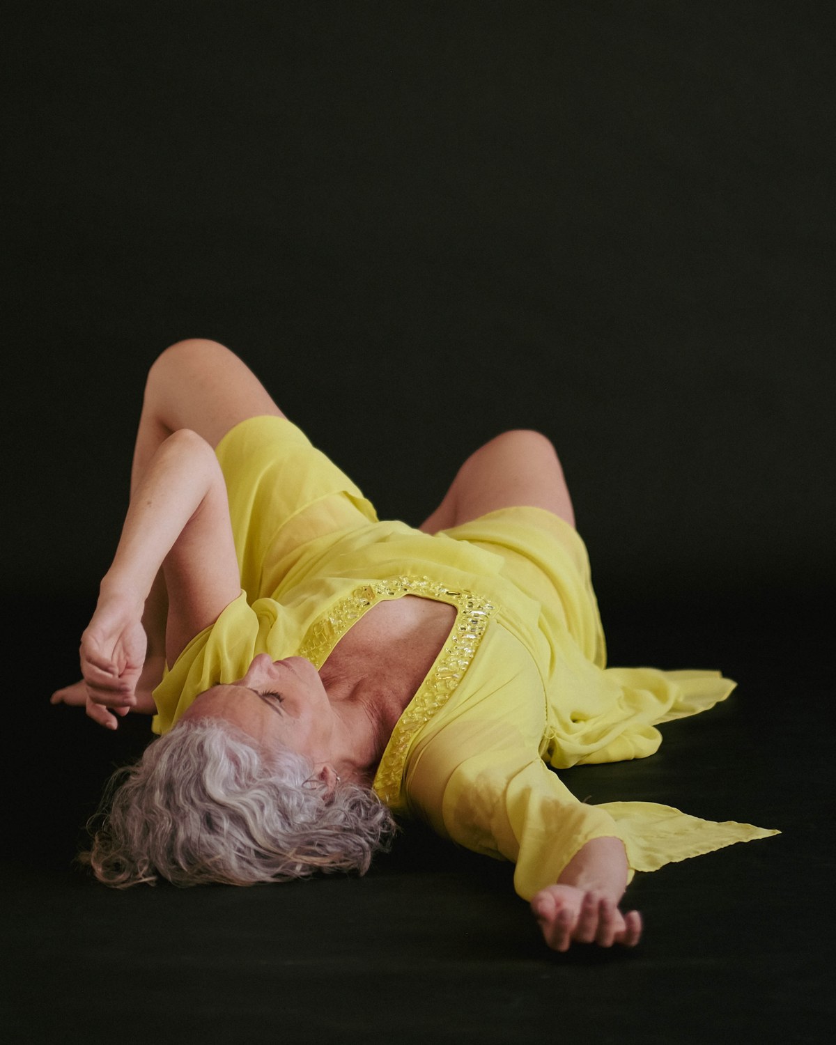 Emmanuelle Em resting on her back in a yellow dress, eyes closed, at peace