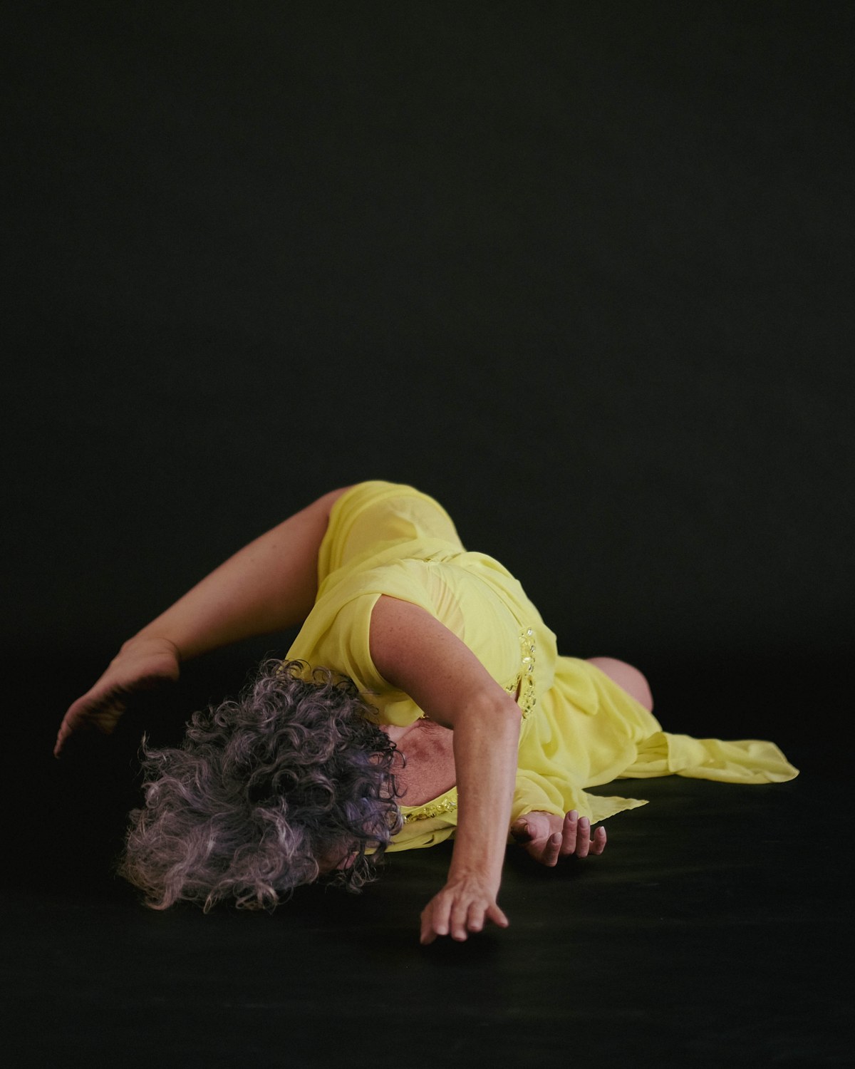 Emmanuelle Em curled on the floor in a flowing yellow dress, intimate and still
