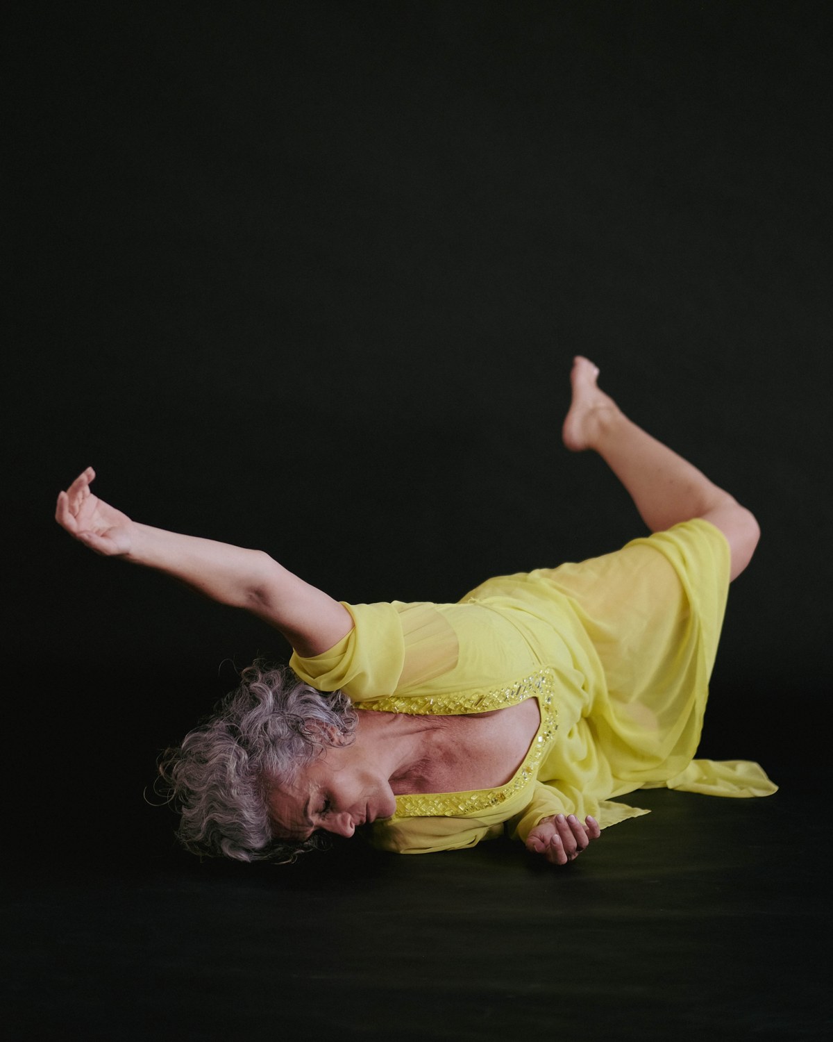 Emmanuelle Em lying on her back in a yellow dress, arms open in a gesture of release